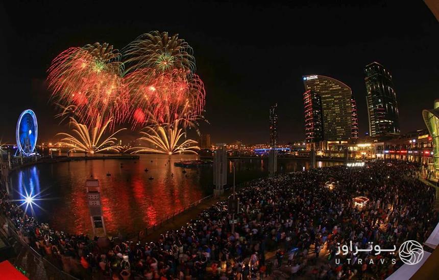 جمعیت ایستاده دور دریاچه‌ای در دبی درحال تماشای آتش‌بازی در آسمان شب